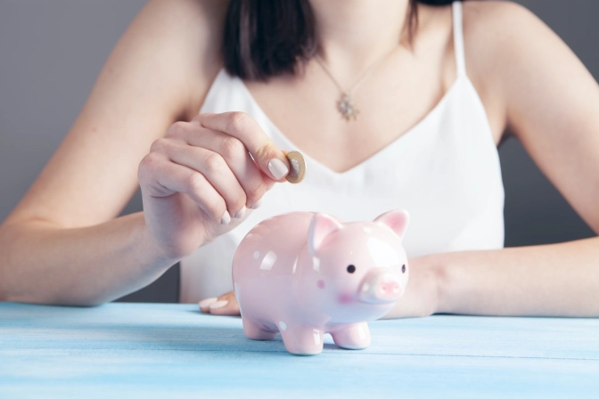 A woman putting a coin in a pink piggy bank