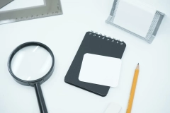 a magnifying glass, a notebook, and a yellow pencil placed on a white table