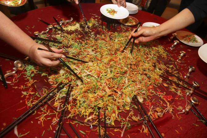 Group of people tossing raw fish salad with black chopsticks