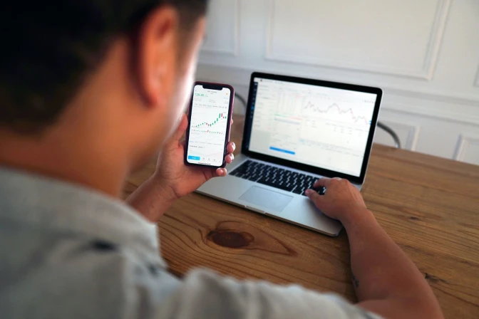 Man in grey shirt holding a phone displaying financial market data