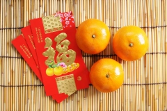 three hong baos and oranges on small wooden stick background