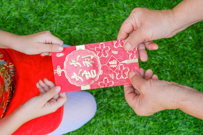 Person giving a red packet to a person in red top and kneeling down on green grass