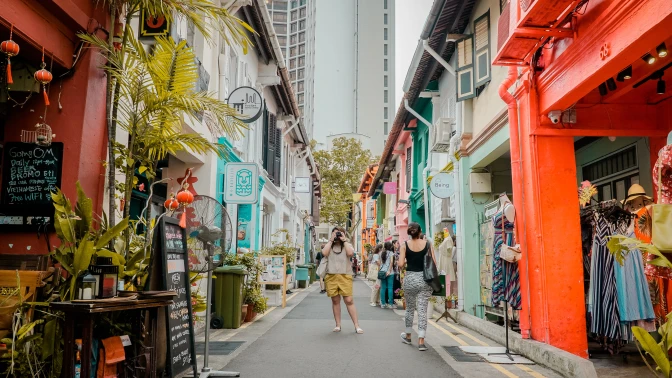 Person standing with a camera along a street of shophouses