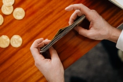 person tidying up a stack of money on a wooden table with several gold coins