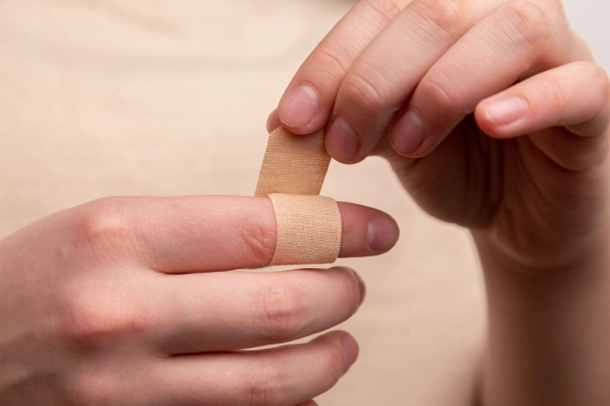 A person wrapping a beige plaster on her injured finger