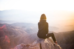 woman sitting on top of rock overlooking mountain view during daytime