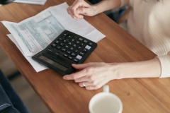 a woman sitting in front of a table with a calculator and pile of paper on top of the wooden table