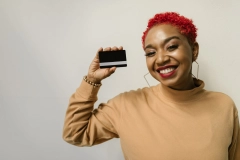 a smiling woman with a mustard turtleneck holding a black card
