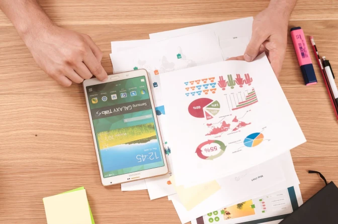 Person holding a white Samsung Galaxy phone alongside graphs and goals document