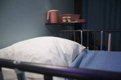 a white pillowcase and blue blanket on a bed with a cup and medicine on the table beside the bed