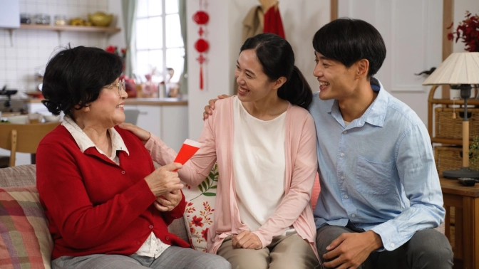 An elderly woman holding a red packet sitting beside a young couple