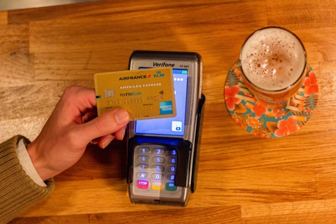 Person holding gold american express credit card against card machine