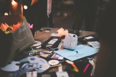 a messy wooden table with a white polaroid and various paper cutouts on top