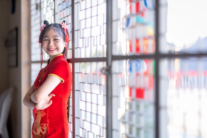 Girl in red Cheongsam leaning against a window pane, smiling at the camera&nbsp;