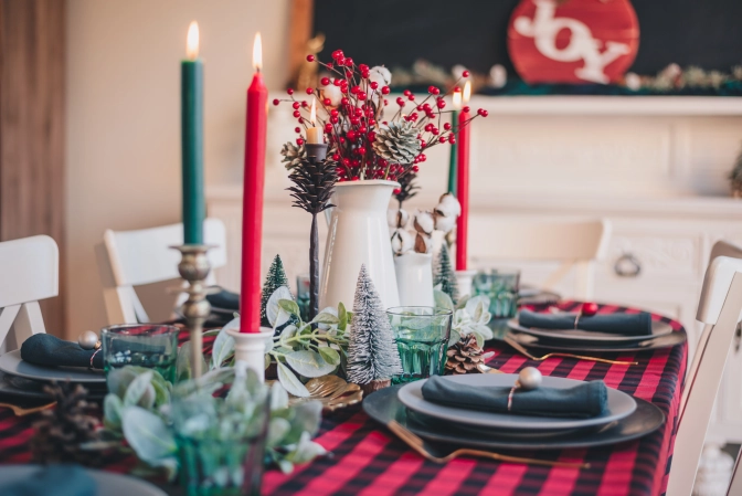 Red and green candles on dining table with Christmas decorations around it