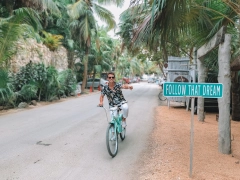 man riding a bike on road while pointing to a sign that says follow your dream