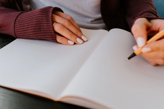 Person in a maroon sweater writing on a notebook